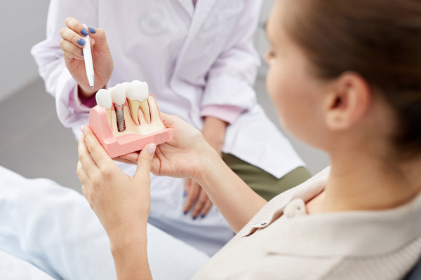 Image of a woman looking at a dental implant model, at Stephen L Ruchlin DDS in Rochester, NY.