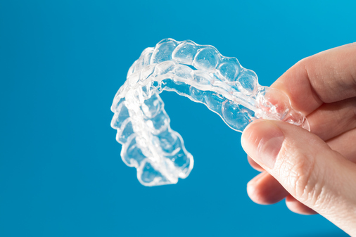 Close up of a hand holding a pair of Invisalign clear aligners