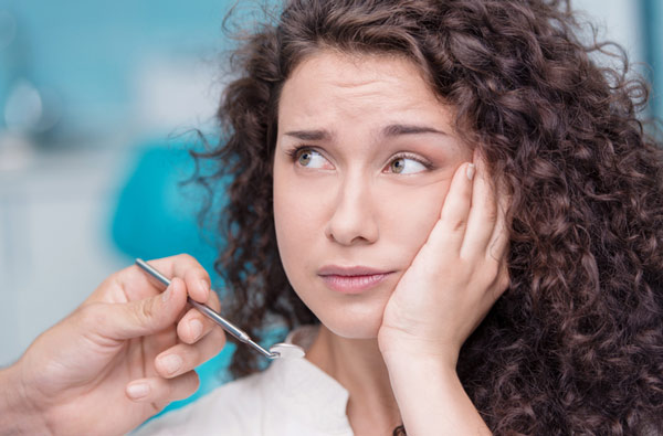 A woman in need of a tooth extraction holding her cheek Stephen L Ruchlin DDS in Rochester.